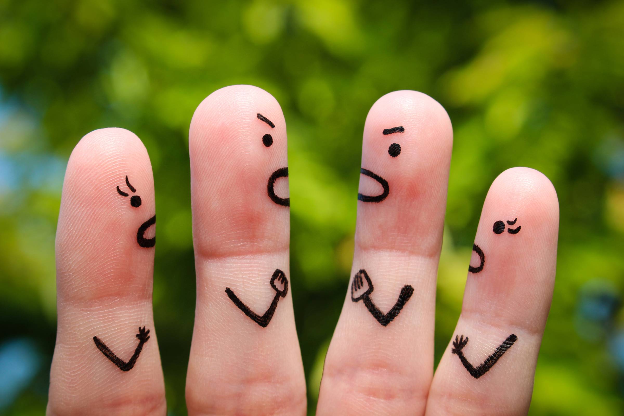 Four fingers with cartoon faces and arms drawn on them, appearing to argue with each other, set against a blurred green outdoor background.