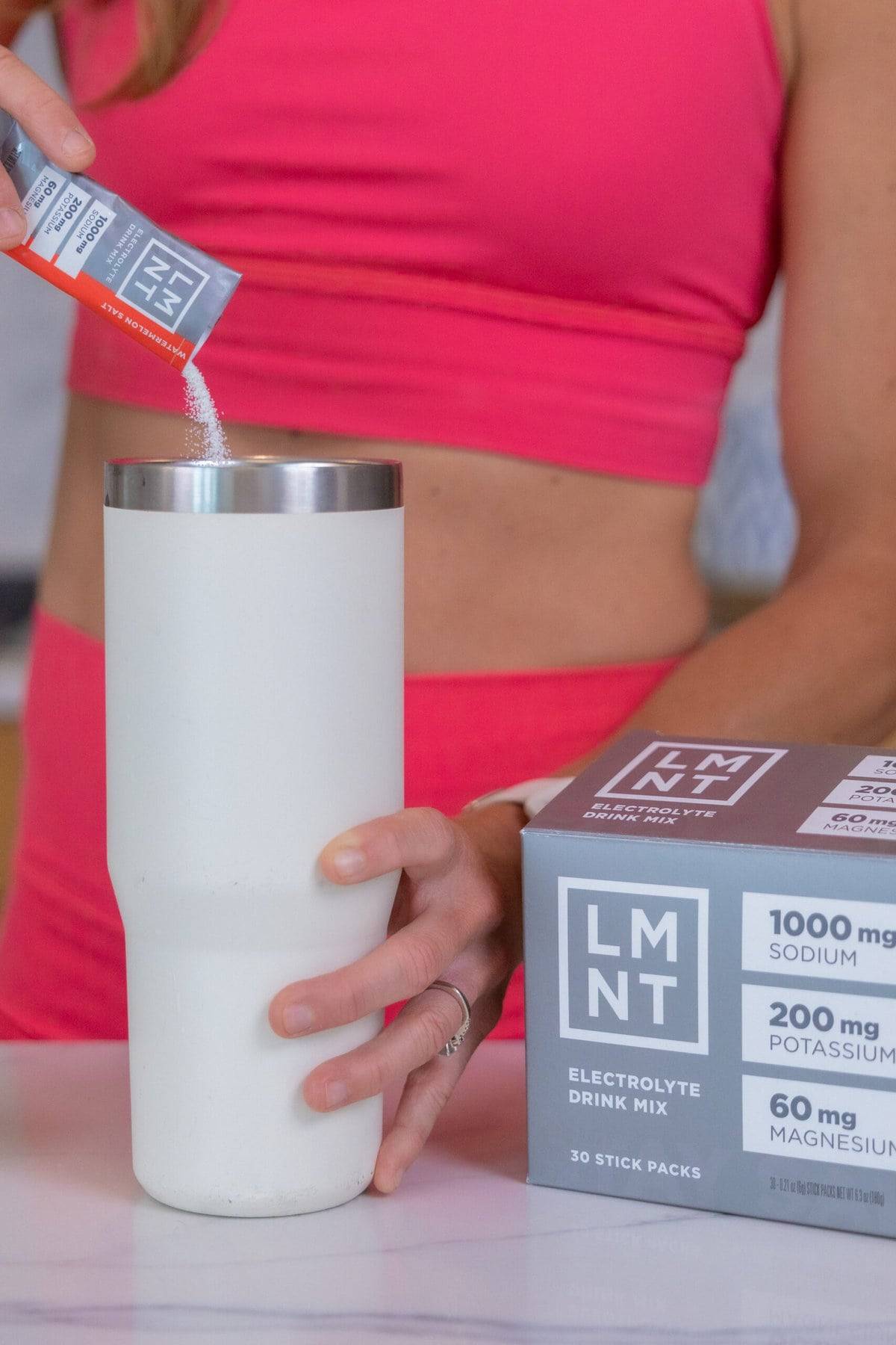 woman pouring LMNT electrolyte drink mix into a water bottle
