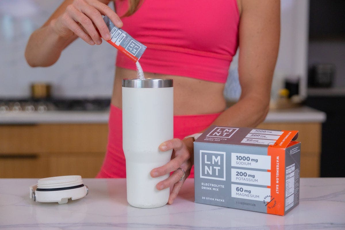 Woman pour LMNT electrolyte into a water bottle in her kitchen.