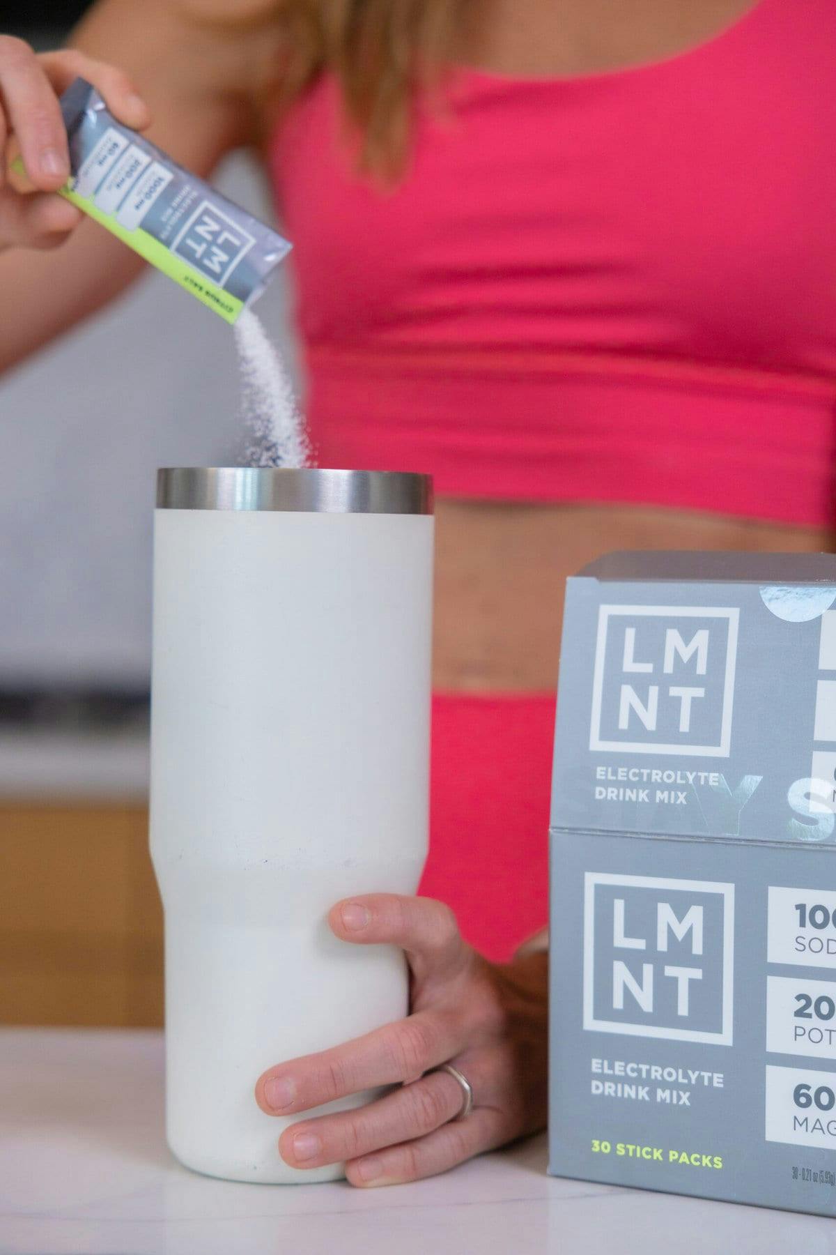 Woman pour LMNT electrolyte into a water bottle in her kitchen.