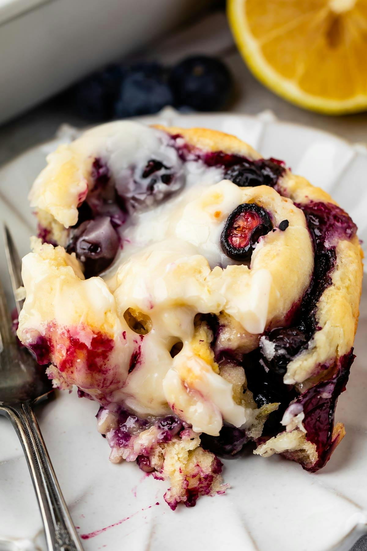 lemon and blueberries mixed in a sweet roll on a white plate next to a fork. 
