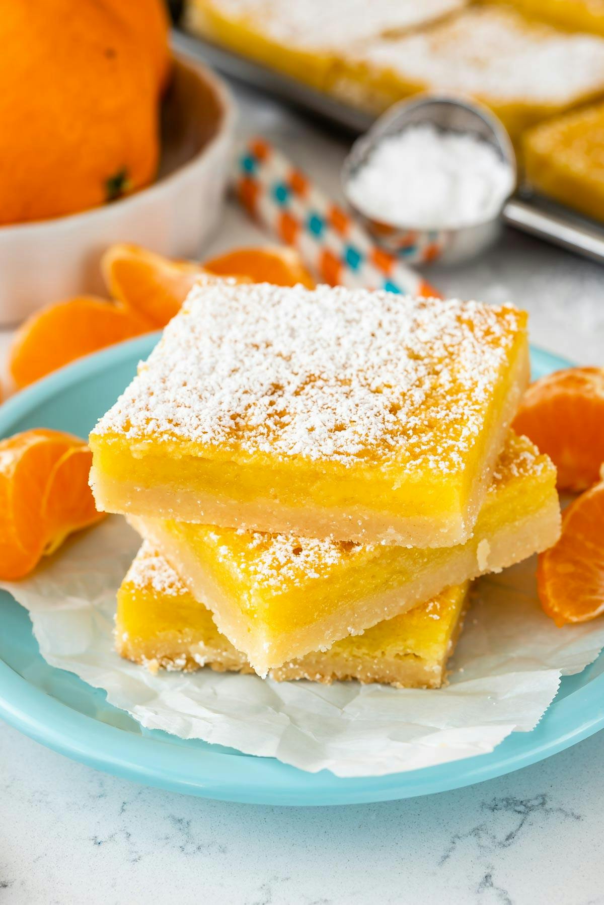 stacked orange bars with powdered sugar on top on a teal plate. 