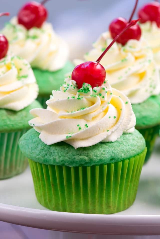 green cupcakes with white frosting and a cherry on top.