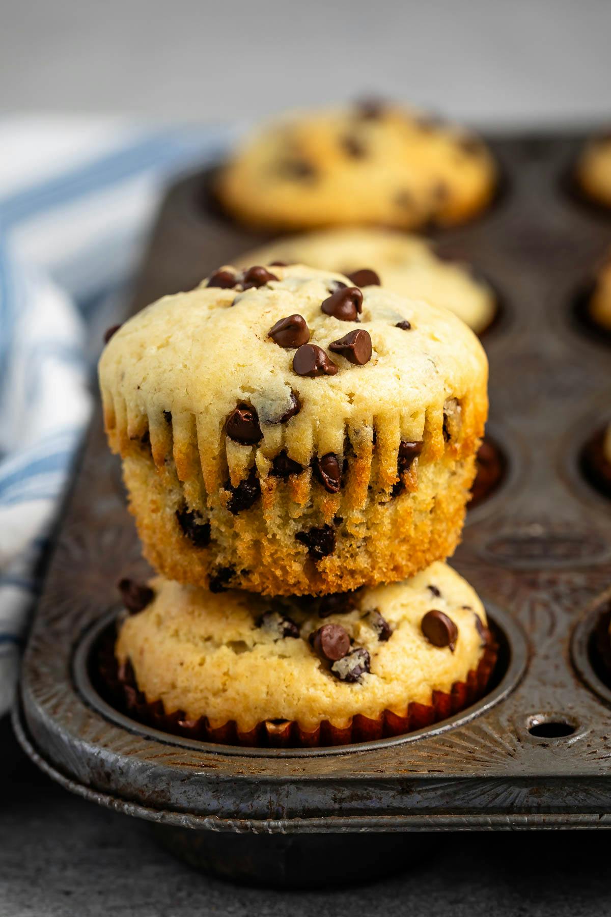 stacked muffins in a grey pan with mini chocolate chips baked in.