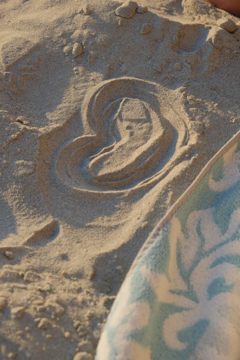 A heart drawn in beach sand with a patterned towel.