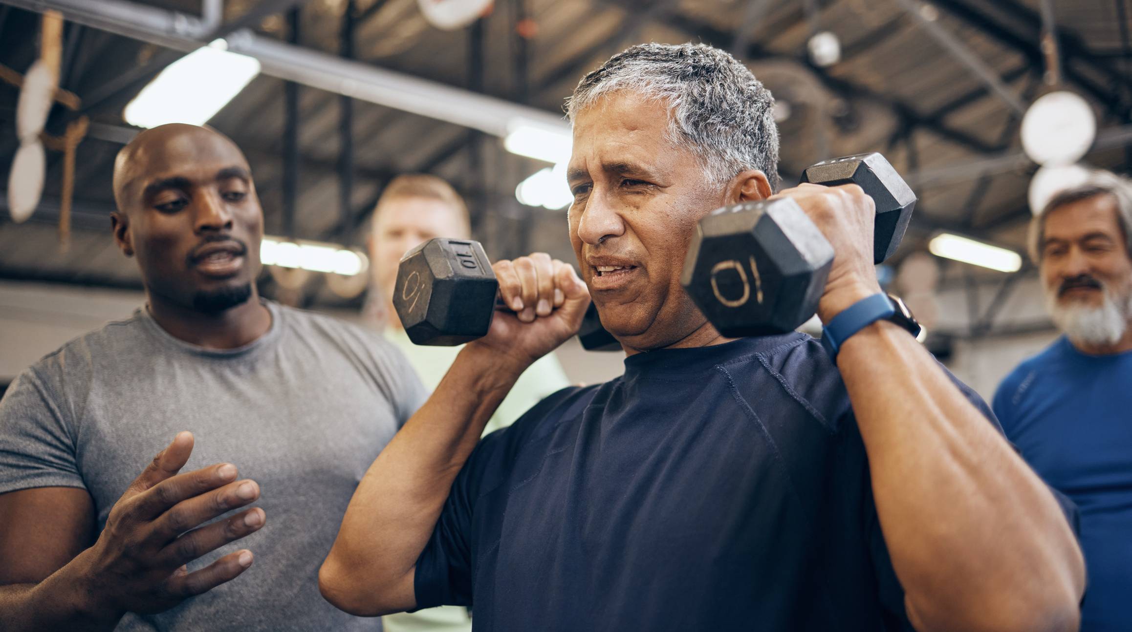 senior man lifting dumbells with help of trainer