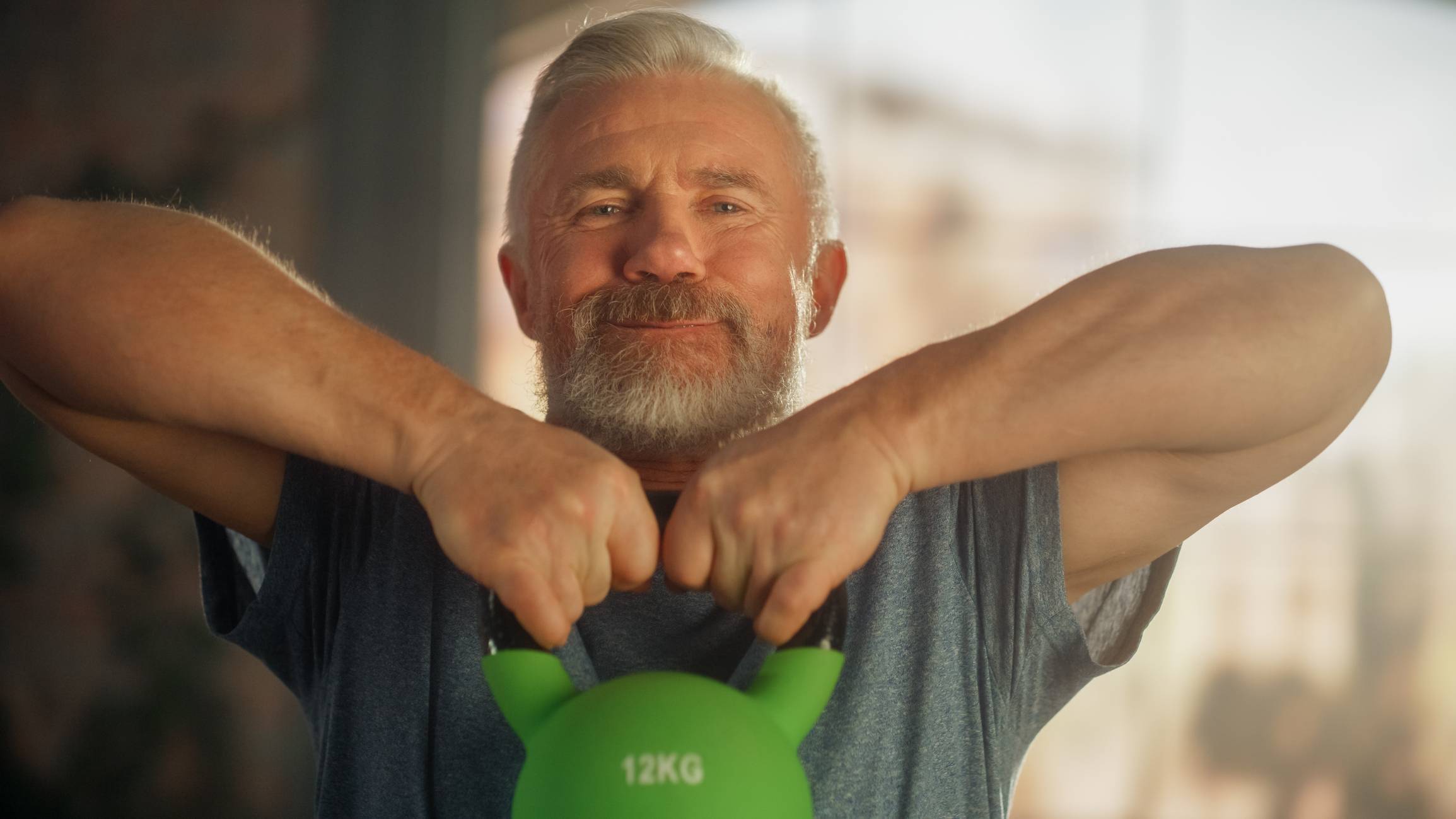 middle aged man lifting a kettle bell and smiling at the camera