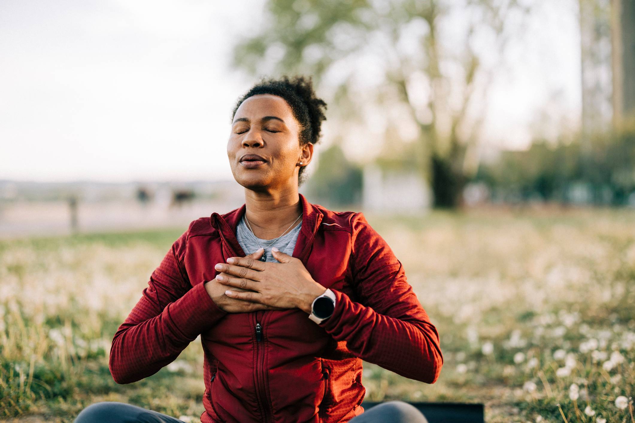 Woman sitting cross-legged performing calming breathing in field