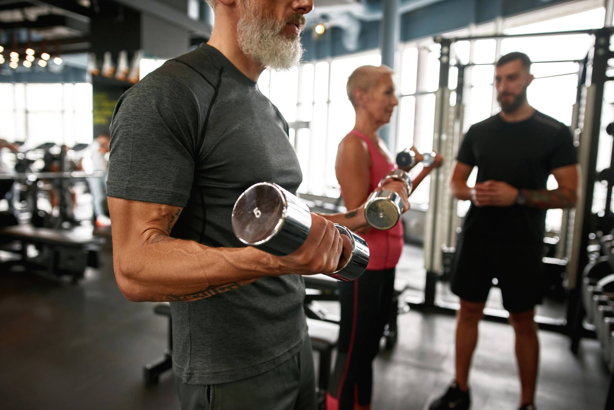 Older Couple at gym lifting dumbells with trainer
