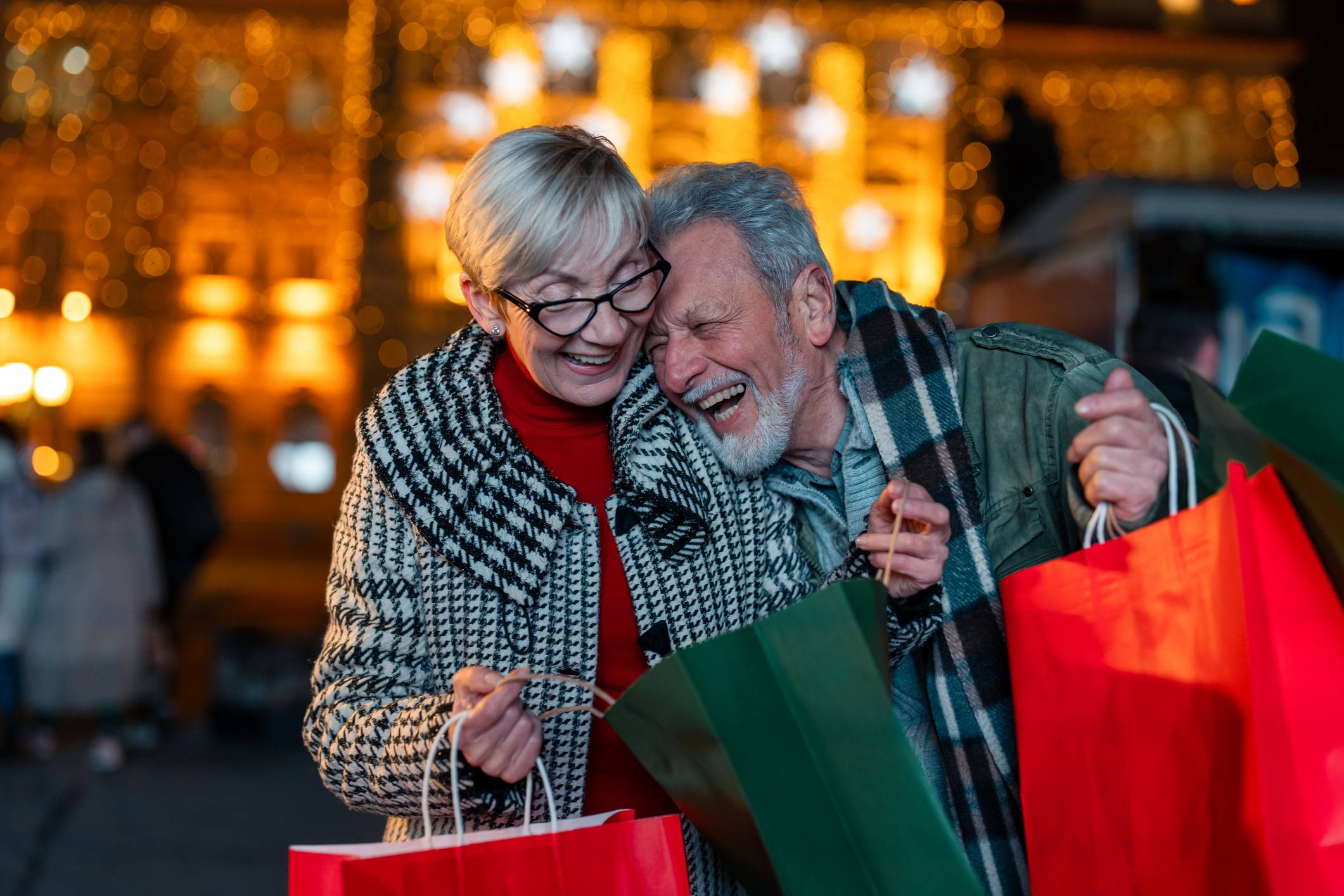 Senor Couple Laughing at Xmas Market with Shopping Bags in Hands