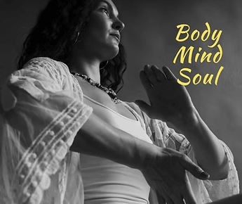 Woman standing in a calm, grounded pose with hands raised near her chest, representing body, mind, and soul connection during a holistic self-care practice.