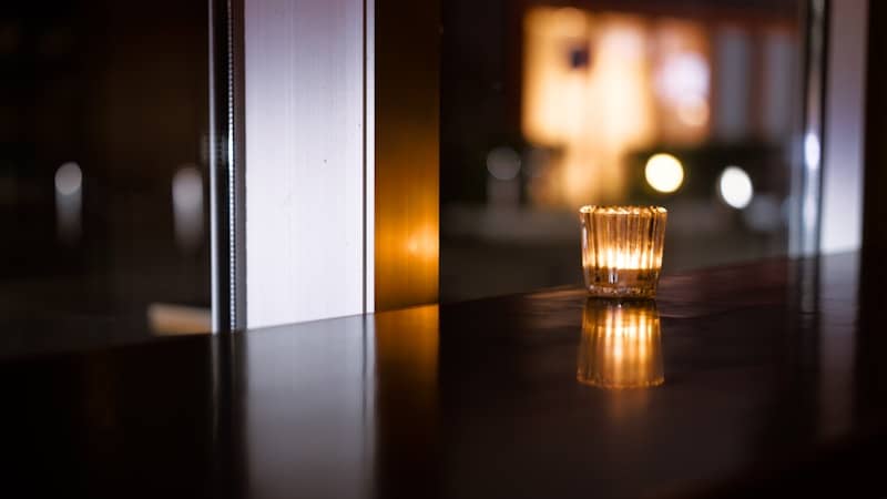 A glowing candle in a glass on a dark table.