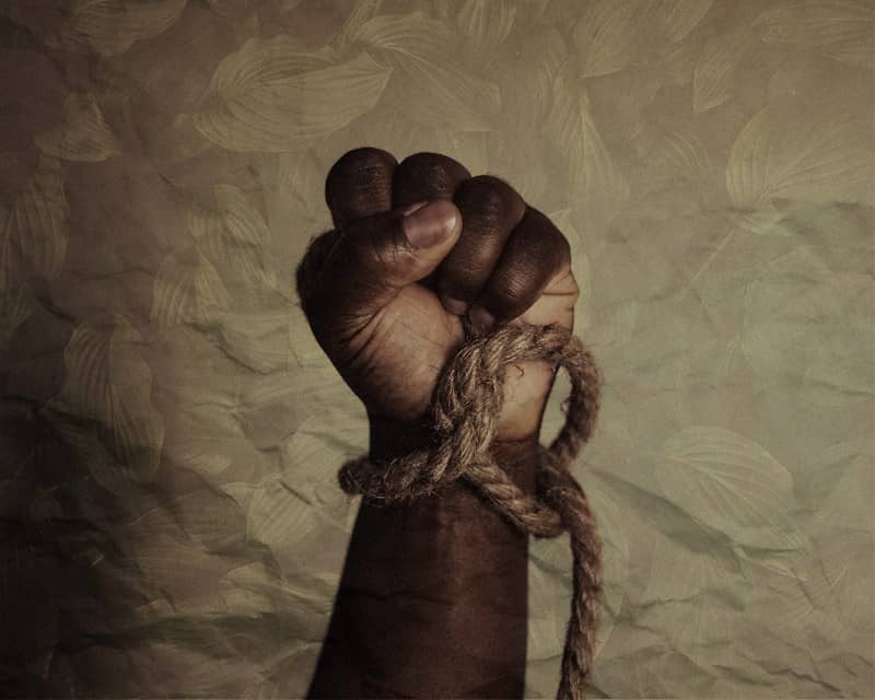 black person's raised fist and wrist tied with rope 