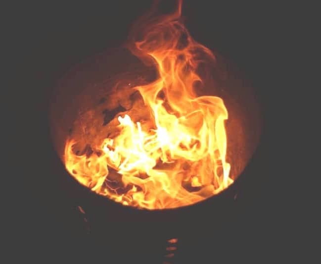 Flames burning intensely inside a dark metal container.