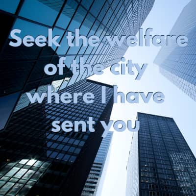 Looking up at tall city building with blue tint words say "seek the welfare of the city where I have sent you"
