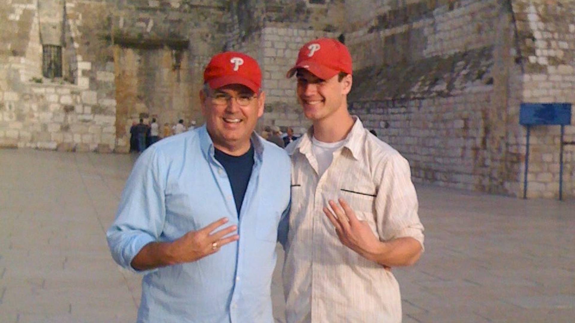 Two men, Dennis and Colin, in front of the Church of the Holy Nativity holding three fingers up