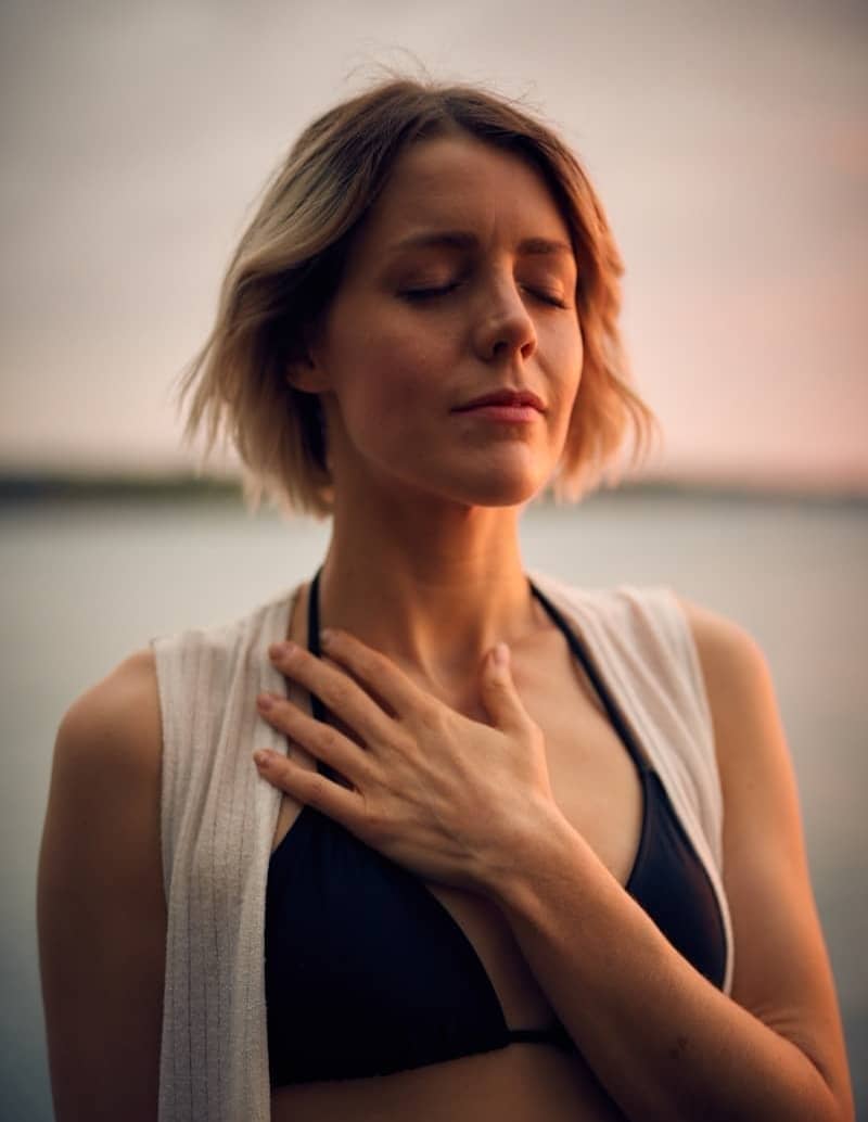 woman in white vest and black bikini with hand on chest