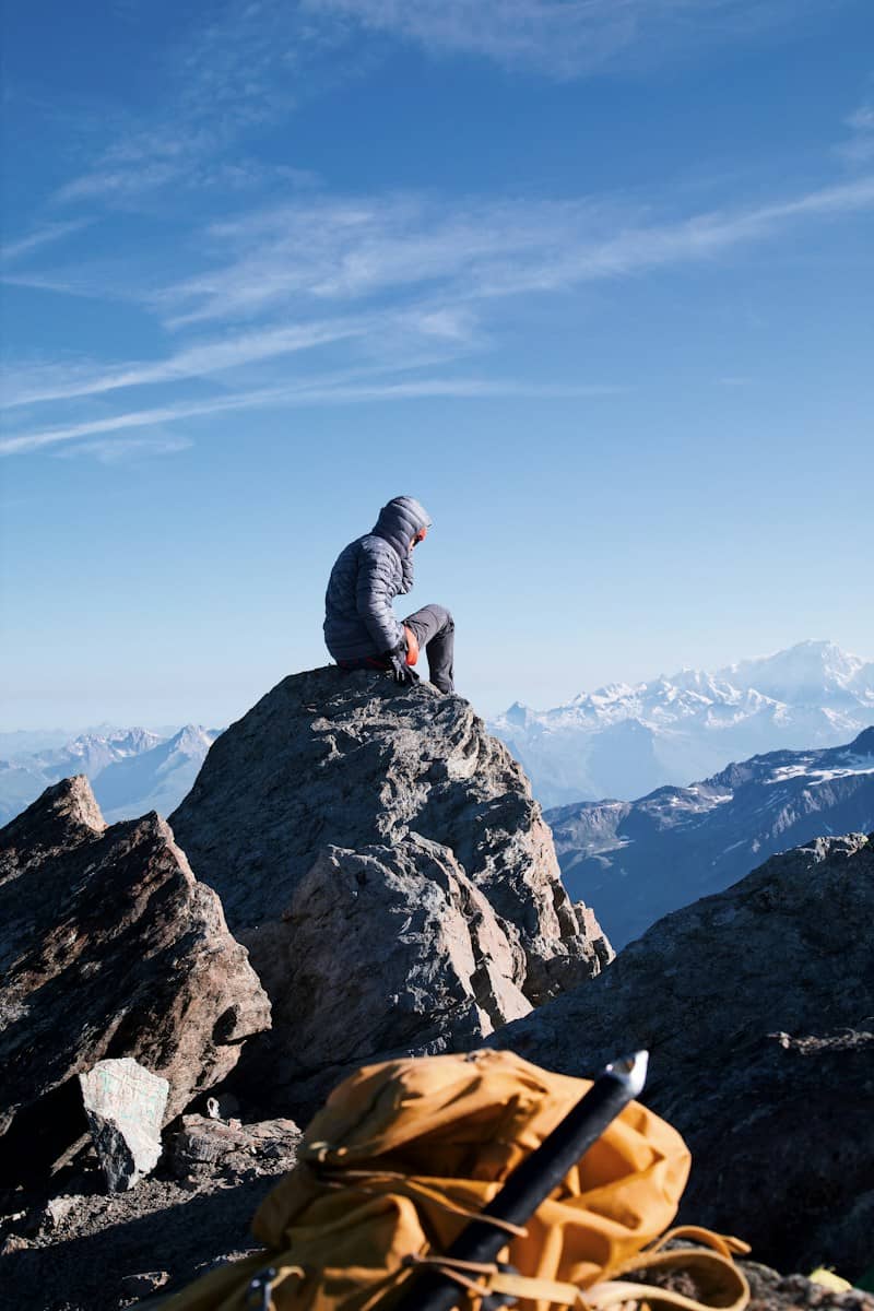 A person in a hooded jacket on a rocky mountain peak under blue sky