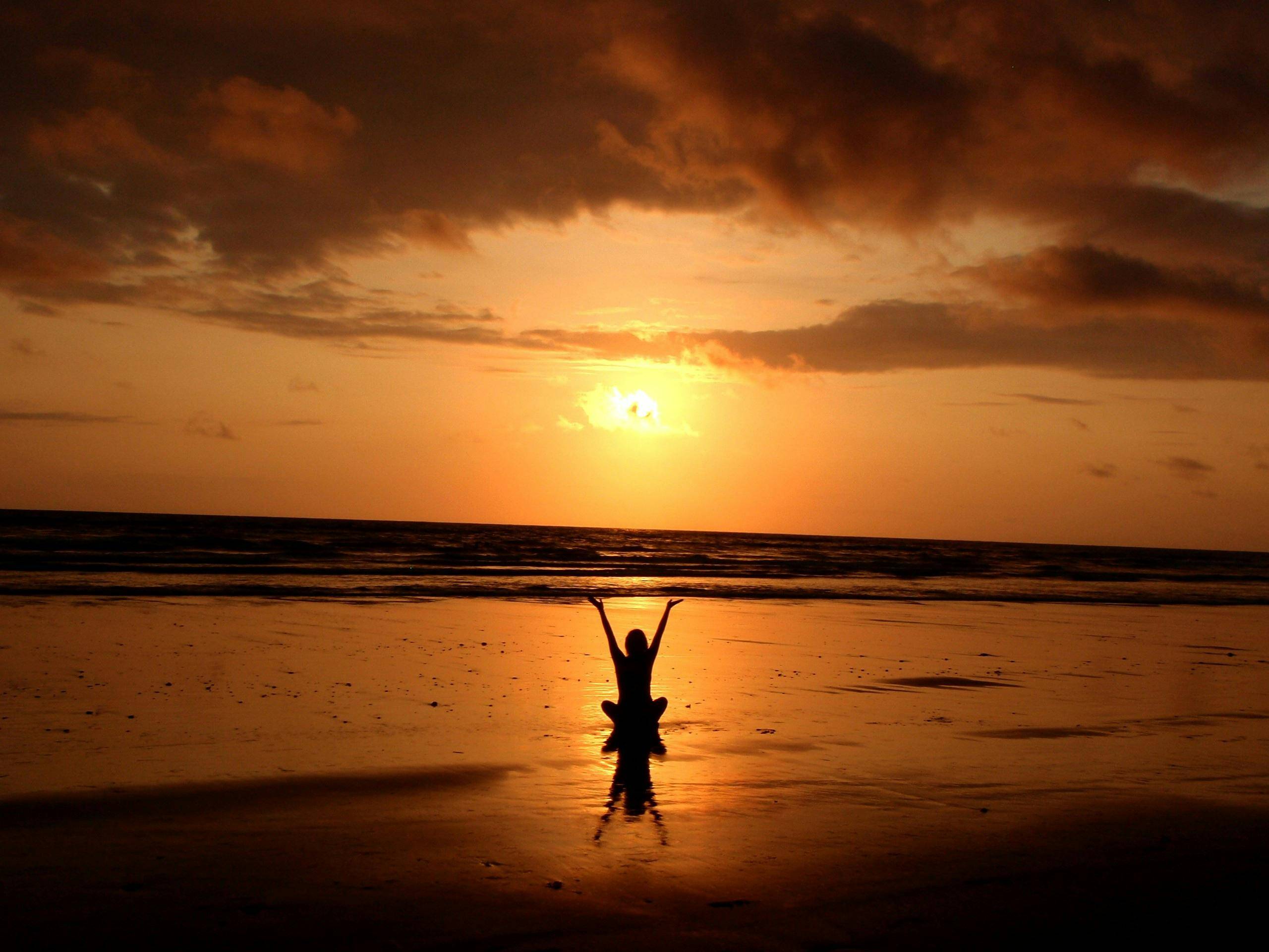 A person sitting on the beach while the sun sets