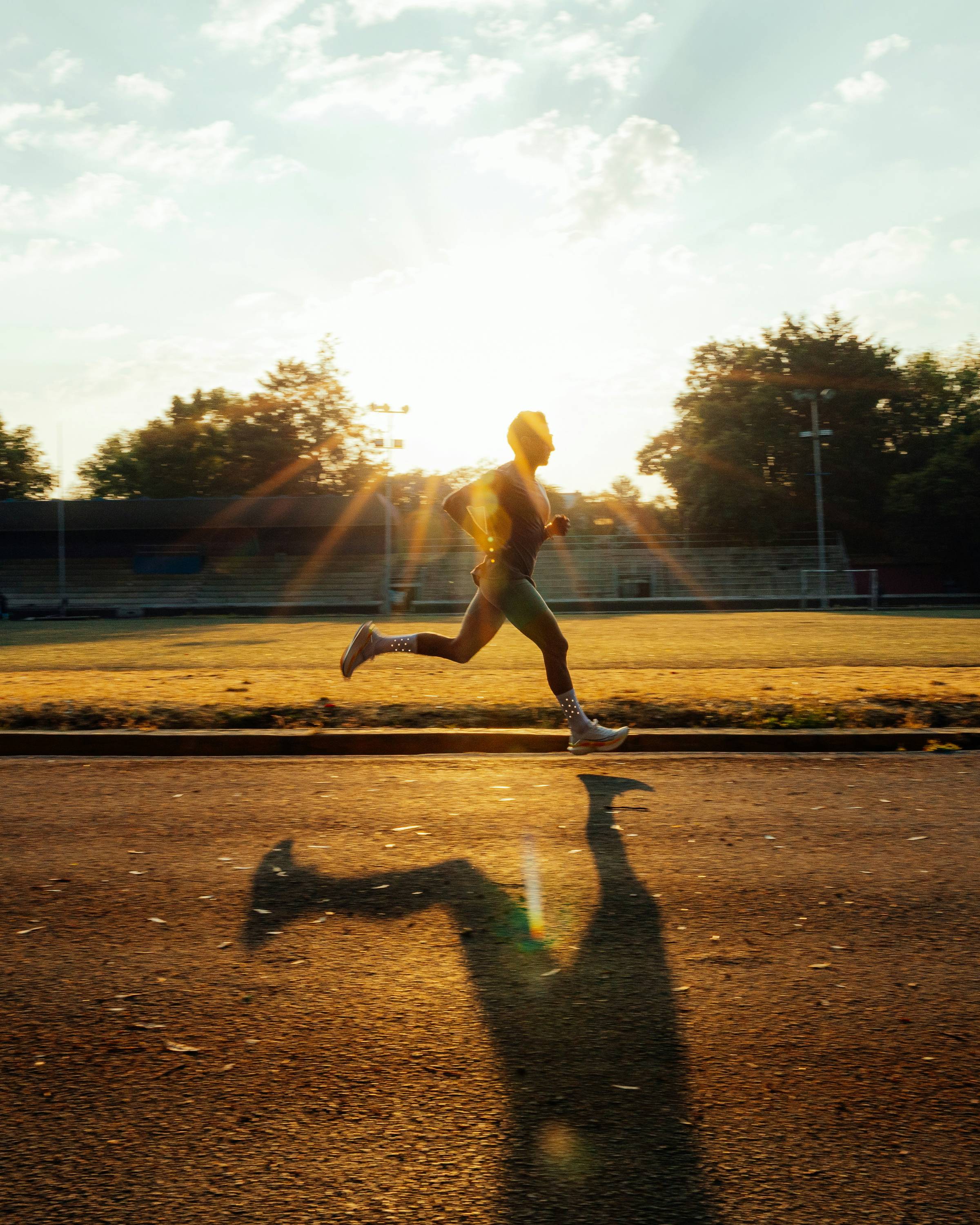 A runner out on a track, backlit by the sunshine