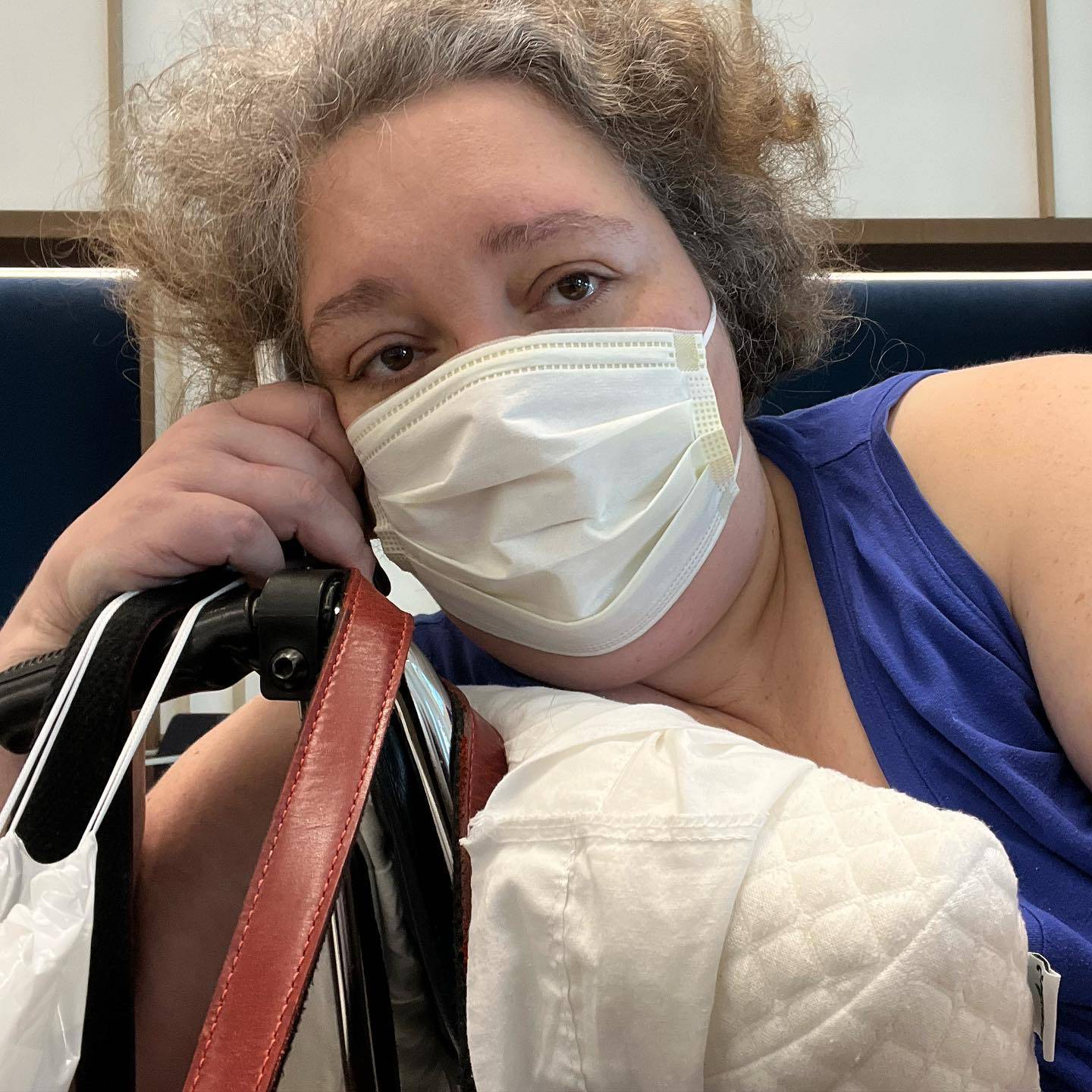 I am leaning into a wheelchair, propped up by a pillow, with my arm hanging over the back. I'm wearing a face mask, and I'm in a LOT of pain.