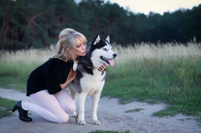 Woman kissing a husky dog in a field.