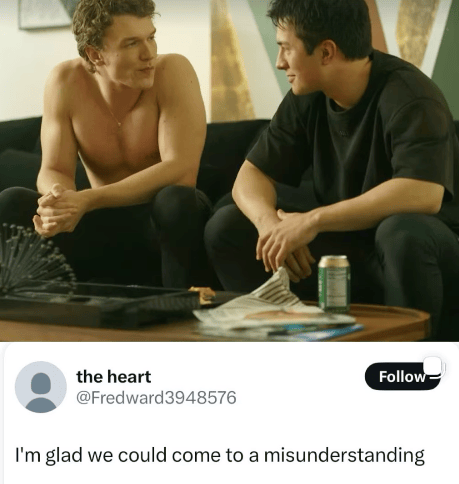 A screenshot combining a TV still with a quote-tweet below it. In the still, two men sit close together on a couch — one shirtless with his hands clasped, looking intently at the other, who wears a black t-shirt and smirks back at him. A coffee table in front of them holds a green can, papers, and a small electric fan. Below the still is a tweet from an account named "the heart" (@Fredward3948576) reading: "I'm glad we could come to a misunderstanding."