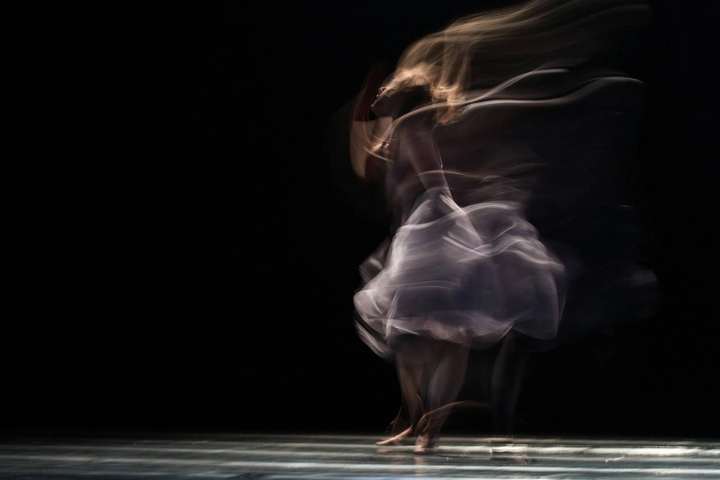A woman in motion, blurred against a dark background, evoking movement and shifting states