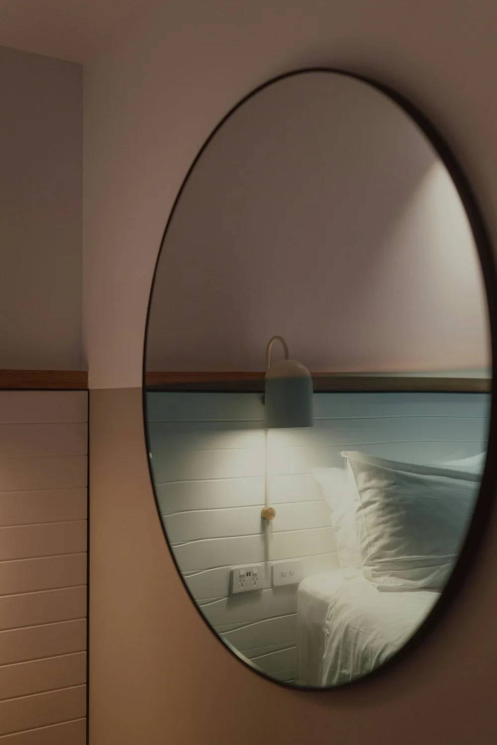 A round mirror reflecting a softly lit wall sconce in a quiet interior