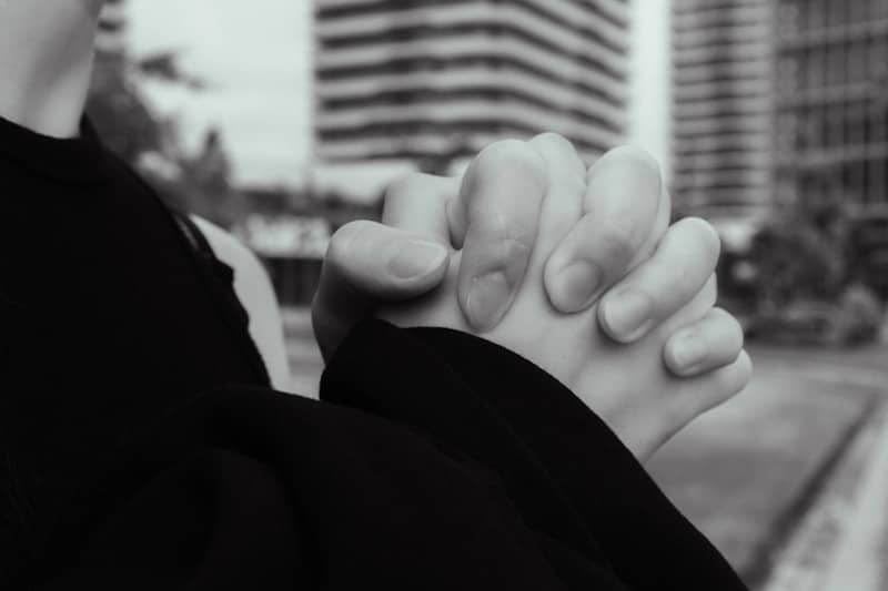 Person clasps hands in prayer, city in the background.
