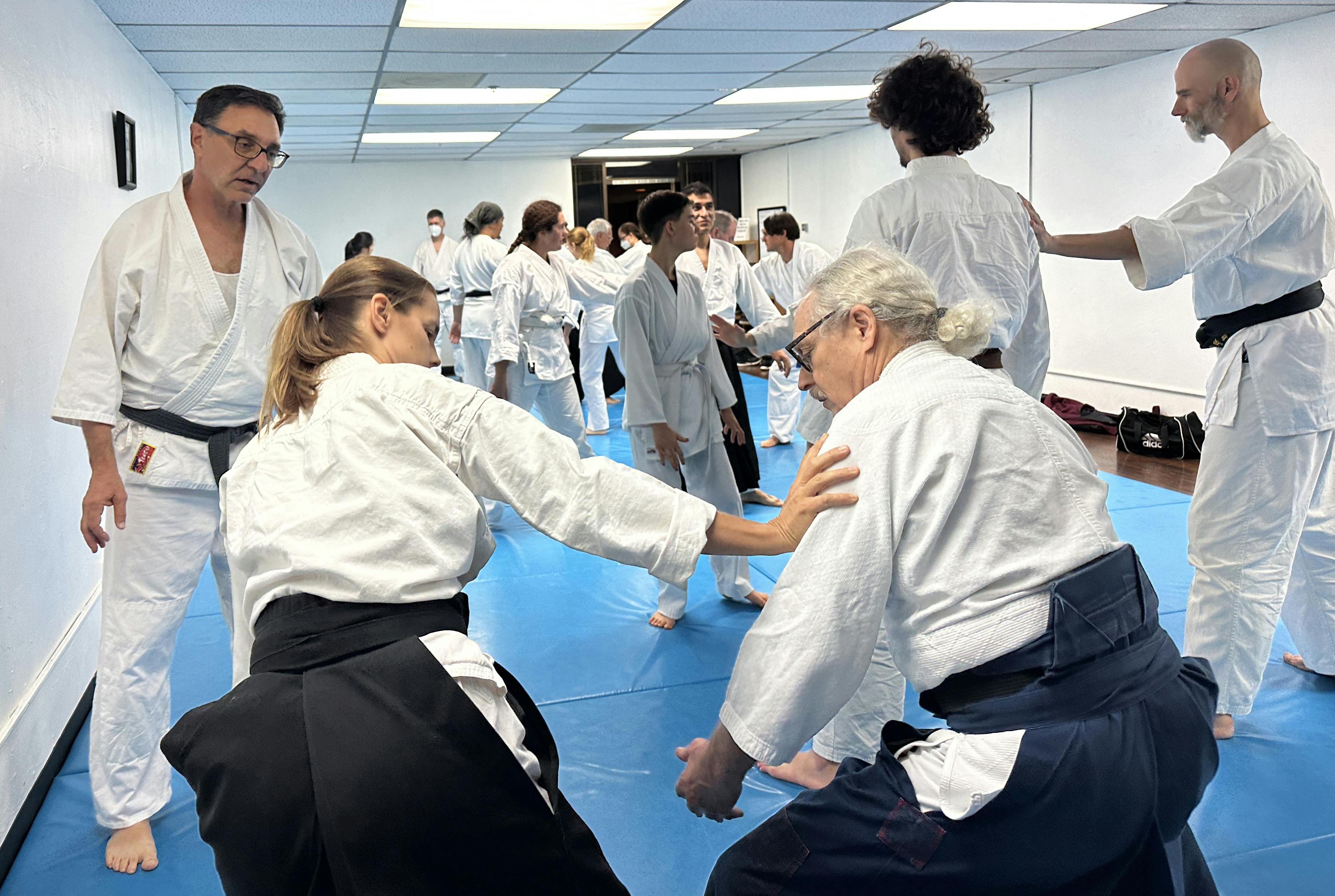 Friends training in a large class on a blue mat at Aikido of San Diego