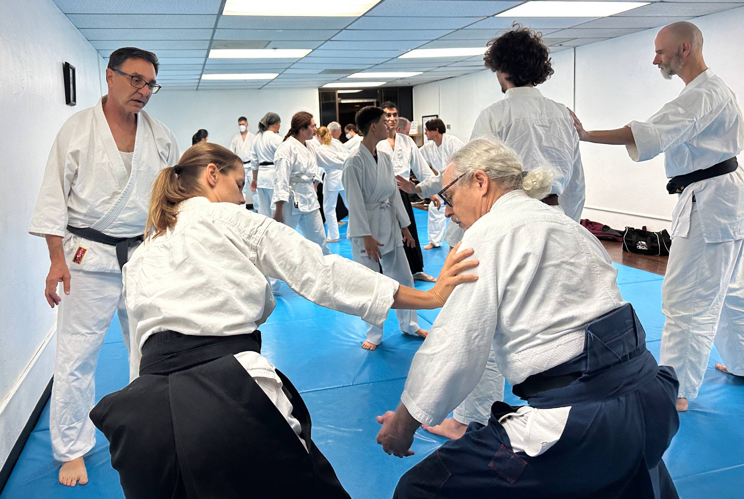 Friends training in a large class on a blue mat at Aikido of San Diego