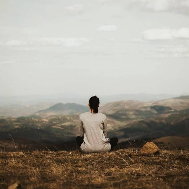 woman sitting on cliff overlooking mountains during daytime