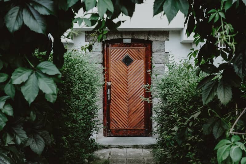 A wooden door is framed by lush greenery.