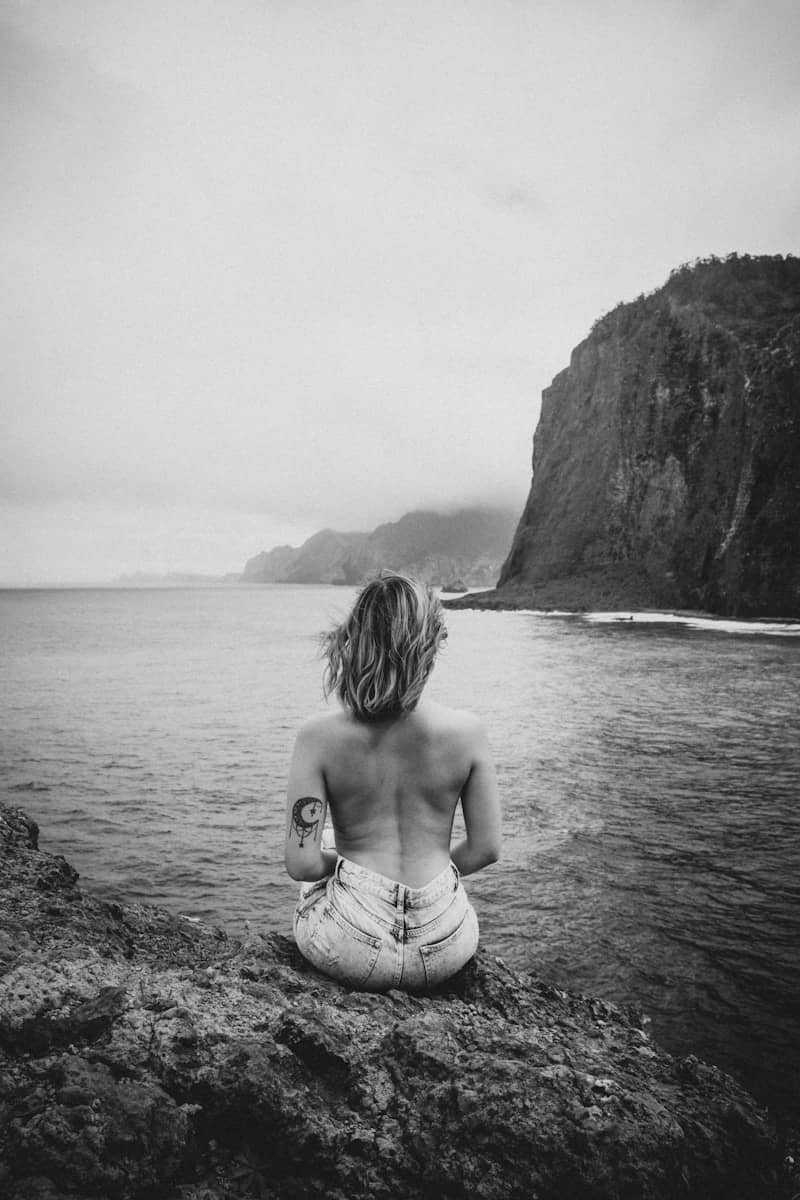 Woman sits on a cliff, gazing at the ocean.