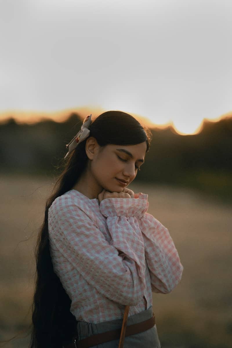 Young woman with long dark hair praying outdoors at sunset.