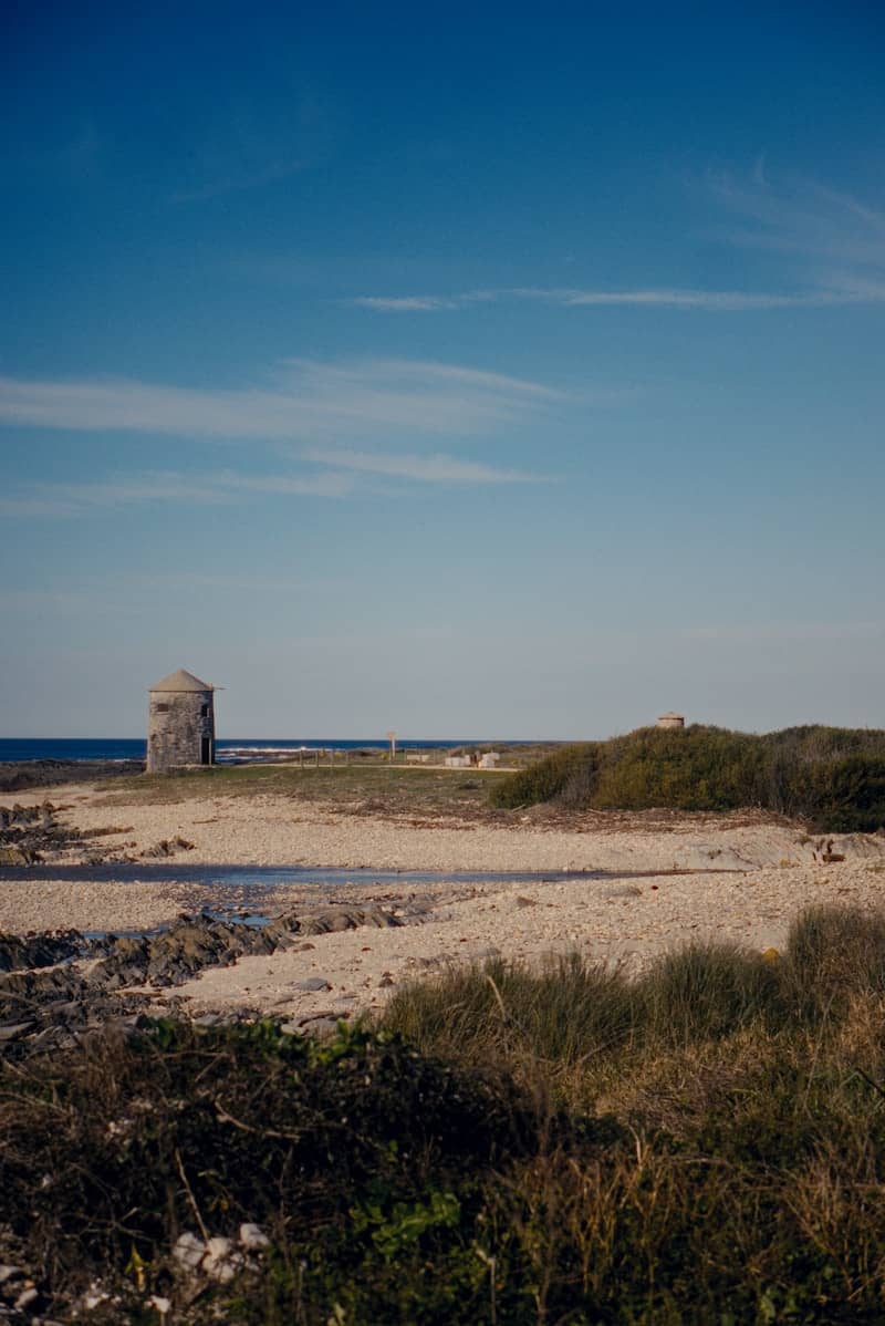Old stone structure on a coastal landscape under blue sky.