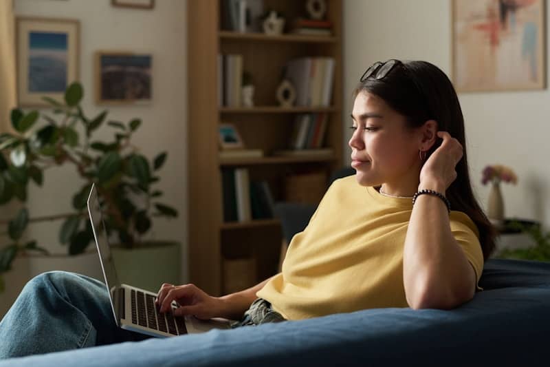 Woman works on laptop while lounging on a couch.