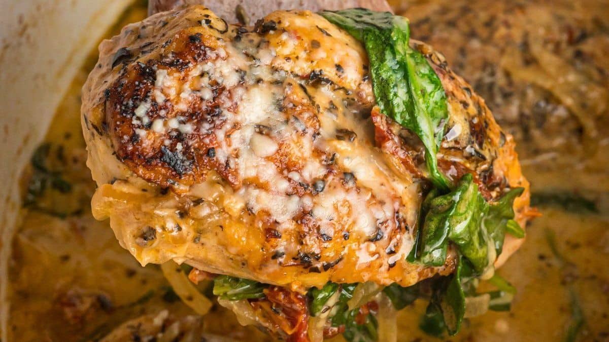 A chicken breast emerging from a slow cooker with sundried tomatoes and a creamy sauce.