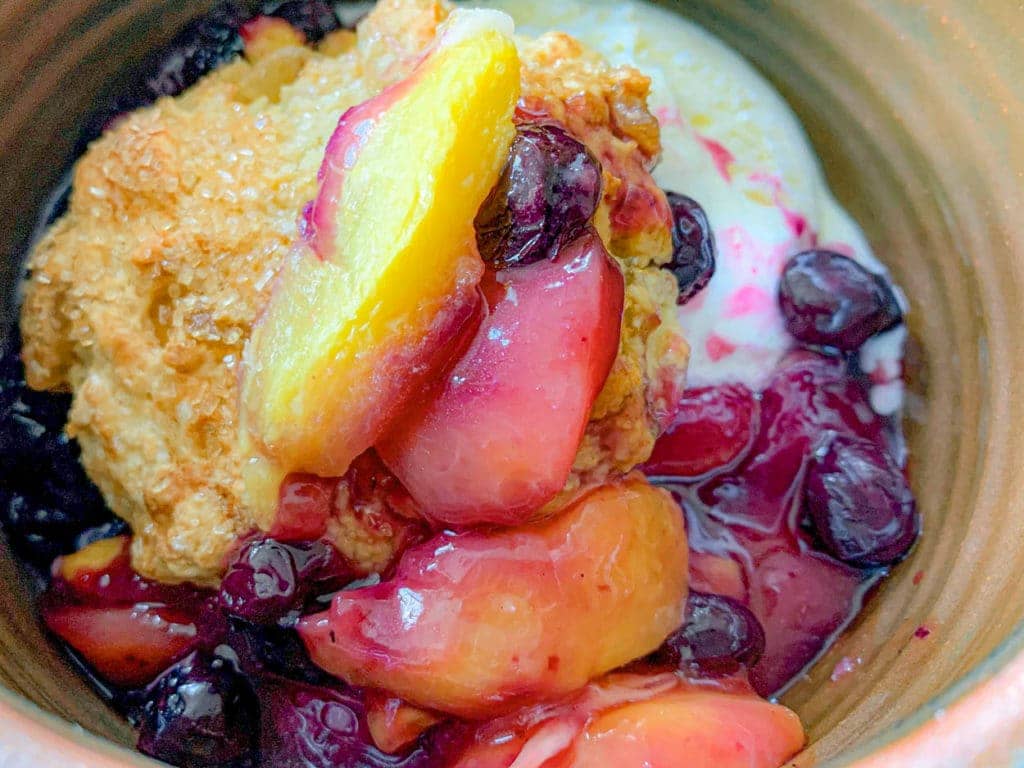Peach cobbler with blueberries and sugary biscuits with ice cream.