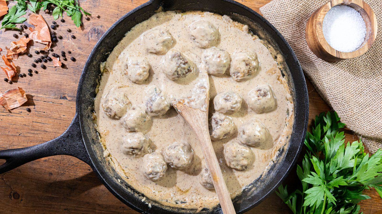 A plate of egg noodles topped with Swedish meatballs, creamy gravy, and crispy fried onions, served on a green-trimmed dish.