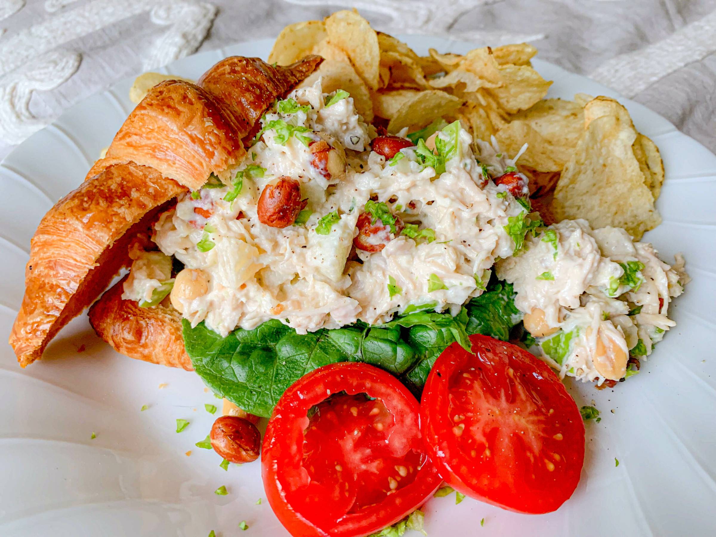 Chicken salad on a croissant with lettuces and slices of tomato.