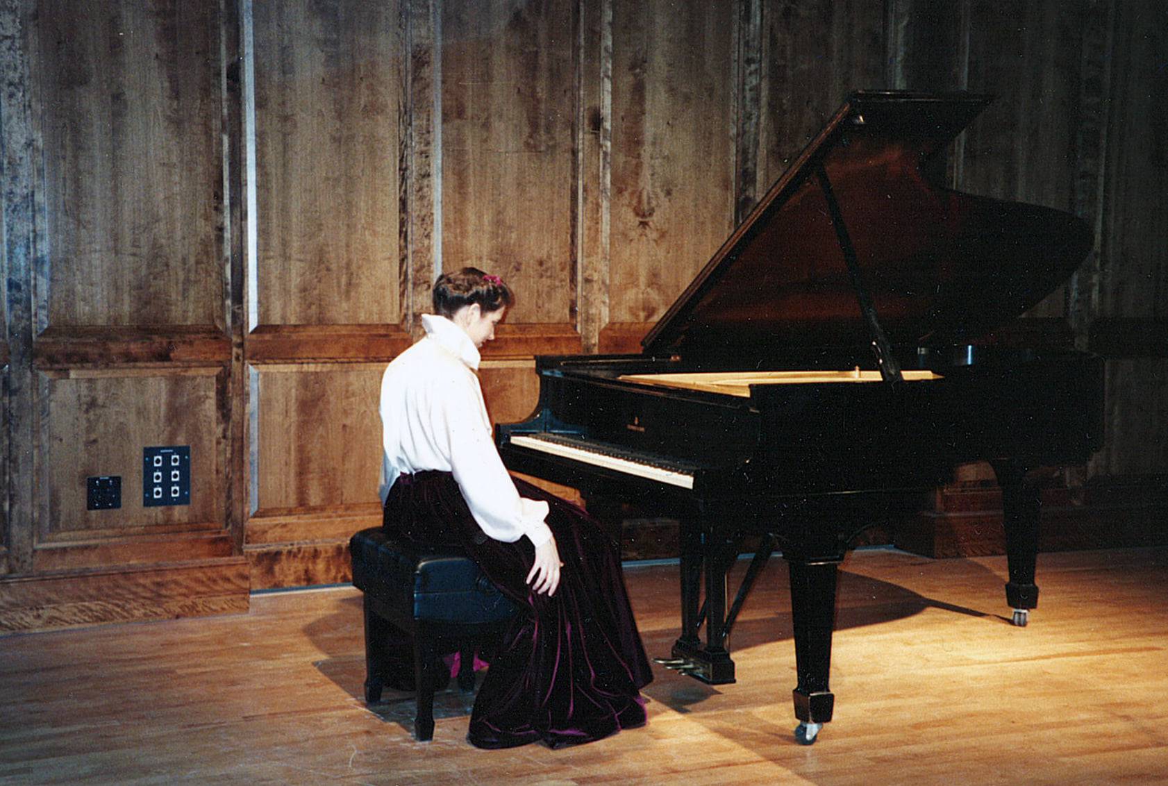 Susanne sitting at a granad piano getting ready to perform in her graduate recital in 1991