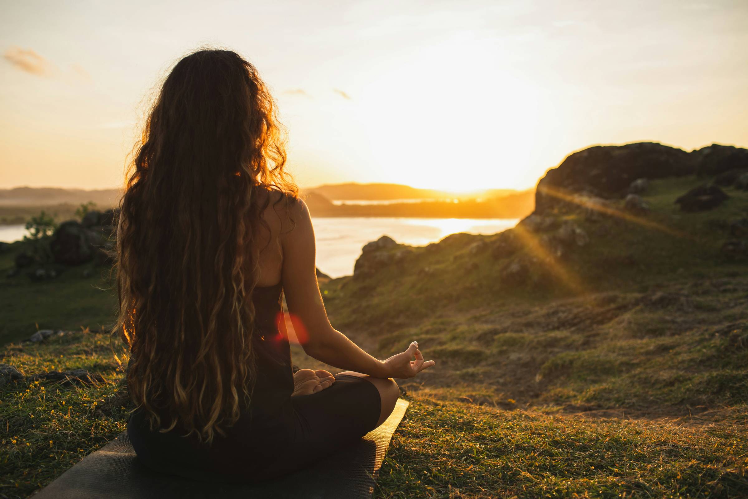 woman meditating by ocean at sunset