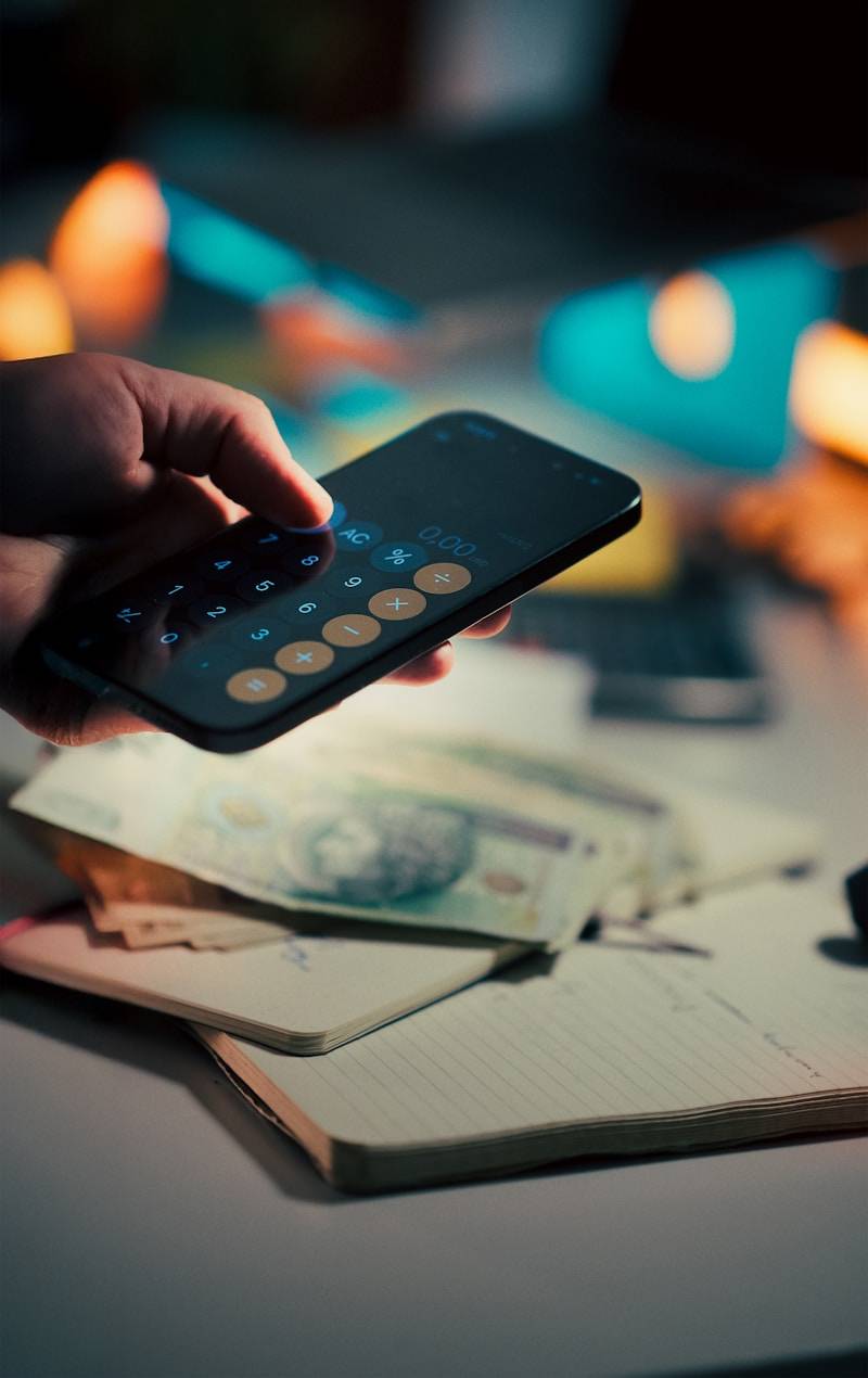 Hand using calculator on smartphone over money.