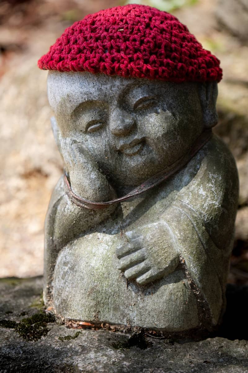 A stone buddha statue wears a red knitted hat.