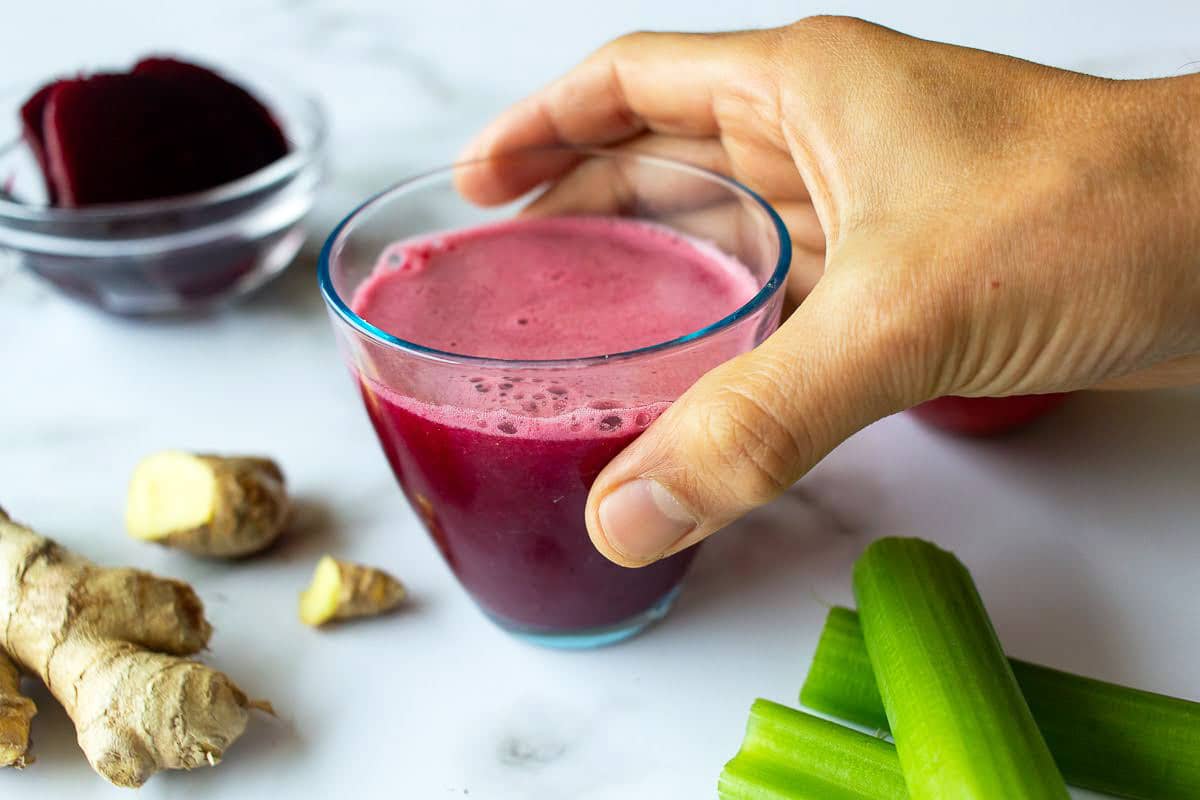 mano levantando un jugo de remolacha antiinflamatorio.