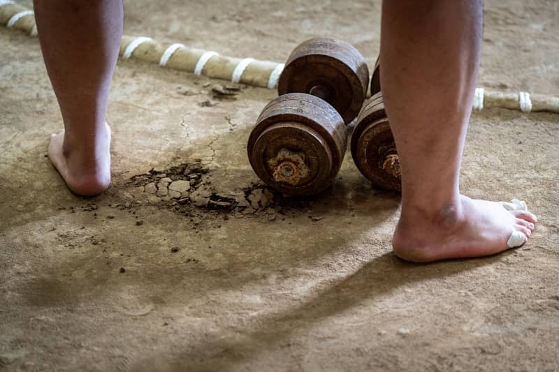 Bare feet near old weights on dirt ground