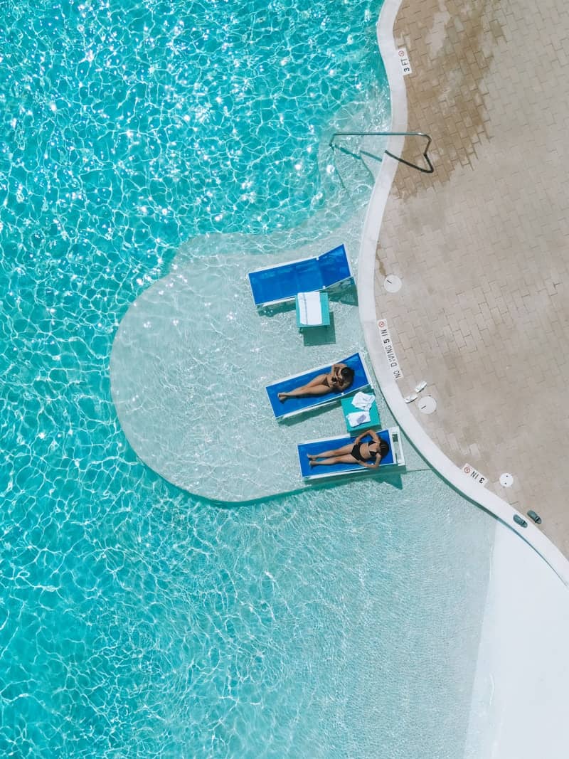 Two people relax on lounge chairs in a pool.