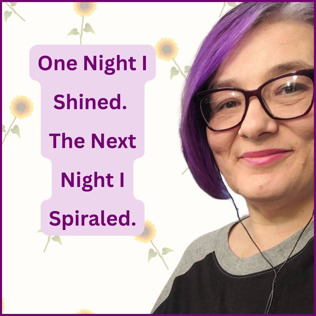 Kat, a woman with purple hair and glasses is wearing a grey and black shirt and smiles at the camera